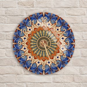 Puede incluir: Un reloj de pared circular con un vibrante patrón de mandala en tonos azul profundo, naranja quemado y crema. La esfera del reloj muestra números dorados del 1 al 12 y manecillas doradas para las horas, minutos y segundos en el centro.