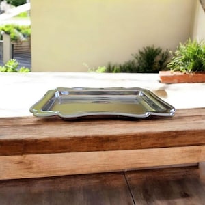 May include: A rectangular, silver-colored serving tray with a scalloped edge. The tray is made of a shiny metal and sits on a wooden surface. The tray is approximately 12 inches long and 8 inches wide.