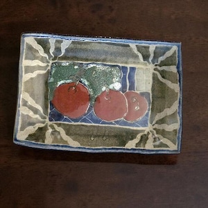 May include: A rectangular ceramic tray featuring a hand-painted design of three red tomatoes on a blue grid surface. The border is decorated with a textured olive green pattern and wavy white lines, finished with a dark blue rim around the edges.