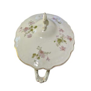 May include: Cream-colored, antique serving dish with a lid. The dish features a scalloped edge and is decorated with pink and green floral patterns. It has a gold trim and a handle on the lid and sides.