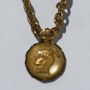 May include: Gold-toned necklace with a circular pendant featuring a profile portrait. The chain is a chunky link design. The pendant has a scalloped edge and a light-colored background.