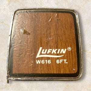 May include: A vintage Lufkin W616 6FT tape measure with a wood-grain design. The tape measure has a metal frame and the Lufkin logo is prominently displayed in white. The text "6FT" is also visible.
