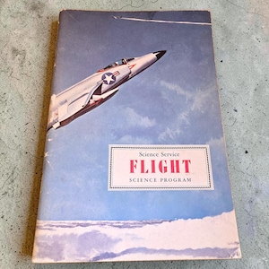 May include: Vintage book cover featuring a jet fighter plane soaring through a blue sky with clouds. The cover has the title "FLIGHT" in red letters, part of the "Science Program" series.