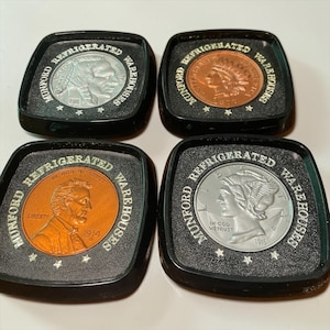 May include: Four vintage Munford Refrigerated Warehouses coasters. Each coaster features a different coin design, including a Native American, a Mercury dime, and a penny. The coasters are black with the company name in white.