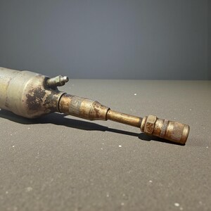 Pode incluir: Uma ferramenta pneum&aacute;tica met&aacute;lica vintage, com um corpo cil&iacute;ndrico e um bico c&oacute;nico. A ferramenta mostra sinais de desgaste, com uma mistura de tons prateados e bronze, e um pequeno bico lateral. O design sugere um uso industrial ou mec&acirc;nico.