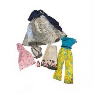 May include: A collection of doll clothing and accessories, including a silver skirt with a navy blue top, a pink dress with heart patterns, a black and white striped top, a cream-colored scarf with black floral designs, a small bottle, and a turquoise top with yellow pants.