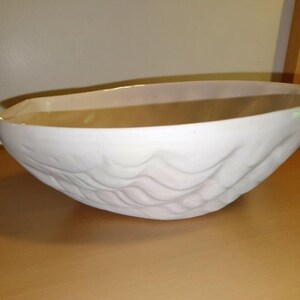 May include: A white ceramic bowl with a textured, wave-like pattern on the exterior. The bowl has a smooth, off-white interior and a wide, shallow design. The bowl is likely used for serving or display.