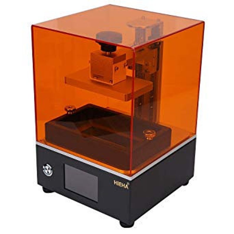 May include: A black 3D printer with an orange resin vat and a clear orange resin tank. The printer has a small LCD screen and a button on the front. The printer is made by the company "HIEHA".