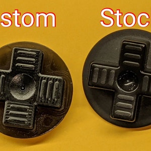 May include: Two black plastic d-pad buttons for a video game controller. The button on the left is labeled "Custom" and the button on the right is labeled "Stock".
