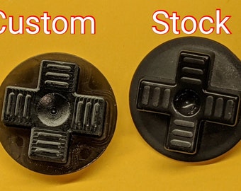 May include: Two black plastic d-pad buttons for a video game controller. The button on the left is labeled "Custom" and the button on the right is labeled "Stock".