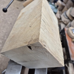 Peut inclure: Un gros bloc de bois brun clair avec un nœud sur un côté. Le bois est posé sur une surface métallique.