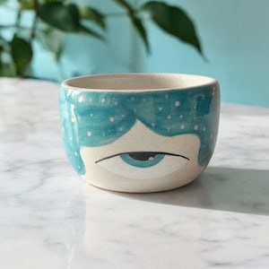 Peut inclure: Un petit bol en céramique blanche avec un motif d'œil bleu et blanc. Le bol est décoré d'un motif en spirale bleu et blanc.
