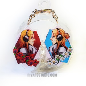 May include: A clear acrylic keychain featuring two mirrored illustrations of a character with long blonde hair and headphones. The left side shows red roses against a dark red background, while the right side displays white roses against a blue background.