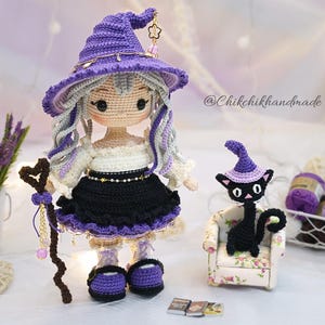 May include: A handcrafted crochet doll wearing a purple witch hat, a white off-shoulder top, and a black skirt with purple trim. The doll has long wavy hair, holds a brown staff, and stands next to a small black crochet cat wearing a purple hat.