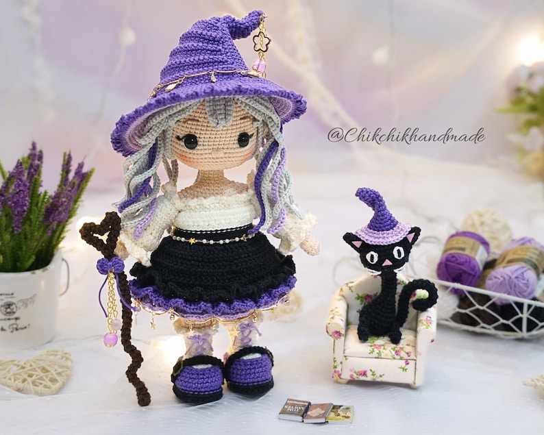 May include: A handcrafted crochet doll wearing a purple witch hat, a white off-shoulder top, and a black skirt with purple trim. The doll has long wavy hair, holds a brown staff, and stands next to a small black crochet cat wearing a purple hat.