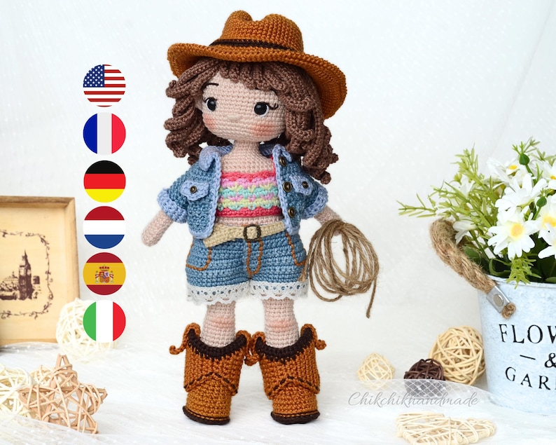 K&ouml;nnte beinhalten: H&auml;kelpuppe mit Jeansjacke, pink-wei&szlig; gestreiftem Shirt, blauen Jeans-Shorts und braunen Cowboy-Stiefeln. Die Puppe hat braunes Haar und h&auml;lt ein Seil.