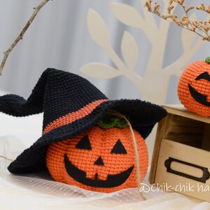 May include: Two crocheted pumpkins, one wearing a black witch hat with an orange stripe. The pumpkins have smiling faces with black eyes and mouths.  The pumpkins are sitting on a wooden shelf with a label that says "Dchik-chik handmade".