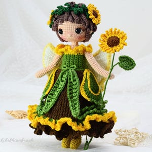May include: Crocheted doll with brown hair, wearing a green and yellow dress with a sunflower crown and holding a sunflower.