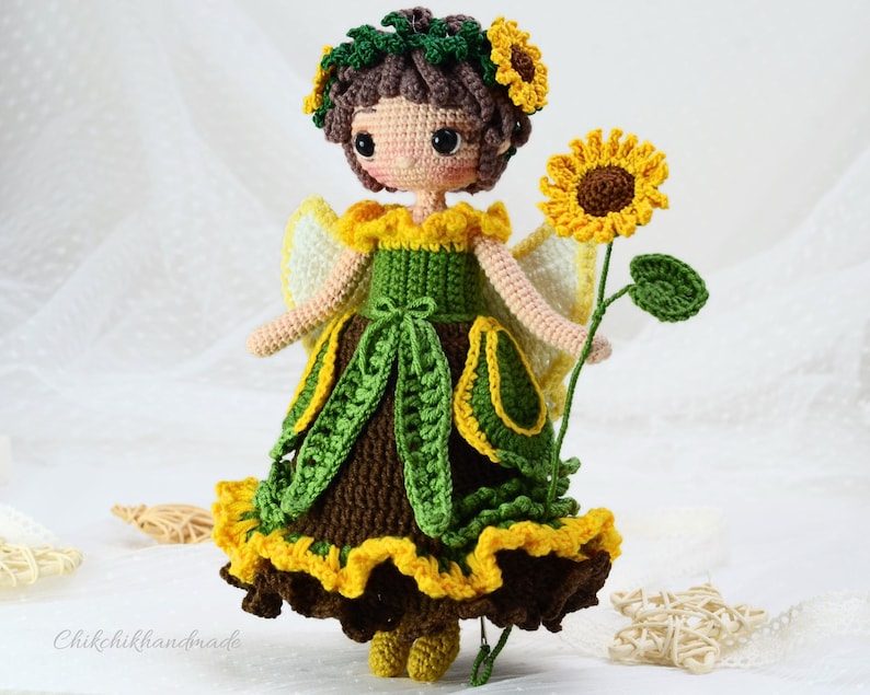 May include: Crocheted doll with brown hair, wearing a green and yellow dress with a sunflower crown and holding a sunflower.