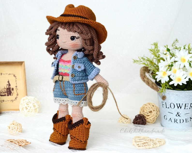 K&ouml;nnte beinhalten: H&auml;kelpuppe mit Jeansjacke, gestreiftem Shirt und braunem Cowboyhut. Die Puppe h&auml;lt ein Seil und tr&auml;gt braune Cowboystiefel.