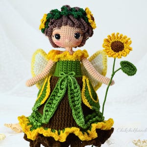 May include: Crocheted doll with brown hair wearing a green and yellow dress with a sunflower in her hand.