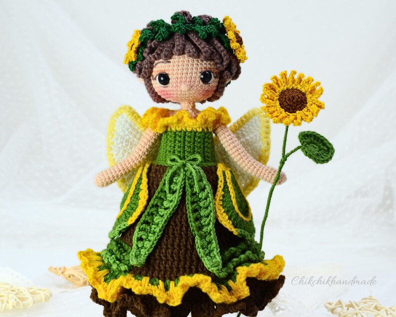 May include: Crocheted doll with brown hair wearing a green and yellow dress with a sunflower in her hand.