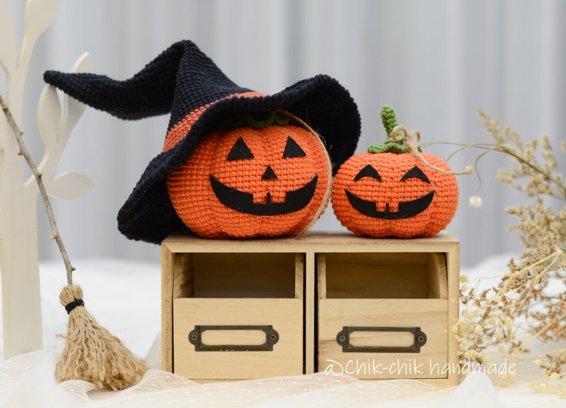 May include: Two crocheted pumpkins, one wearing a black witch hat, sitting on a wooden shelf with two drawers. The shelf has a label that says "@chik-chik handmade".