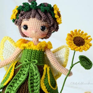 May include: A crocheted sunflower fairy doll with a green dress, yellow and white wings, and a sunflower in her hand. The doll has brown hair and a sunflower crown.