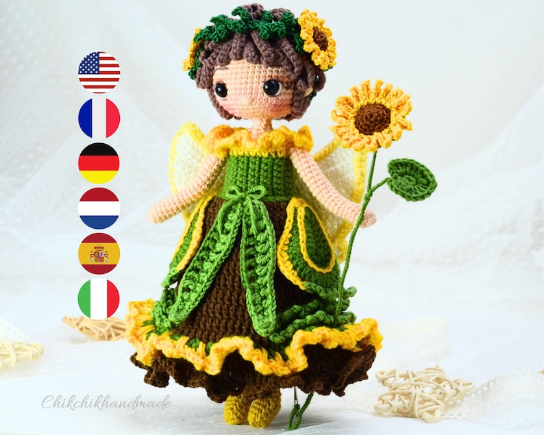 May include: A crocheted doll with brown hair, wearing a green and yellow dress with a sunflower design. The doll is holding a sunflower stem in her right hand. The doll is standing on a white surface.