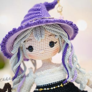 May include: A handcrafted crochet doll featuring light gray hair with purple accents, wearing a pointed purple hat with a gold star charm. The doll has black button eyes, a white top, and a black skirt with a gold beaded belt. Text reads @Chikchikhandmade.