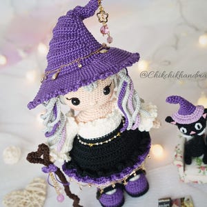 May include: A handcrafted crochet doll wearing a purple pointed hat with gold charms, a white blouse, and a black skirt, holding a brown staff. Beside the doll is a small black crochet cat wearing a matching purple hat. The text @Chikchikhandmade is visible.