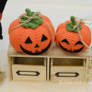 May include: Two crocheted orange pumpkins with black eyes and mouths, sitting on a wooden shelf with a label that says "Dchik-chik handmade".
