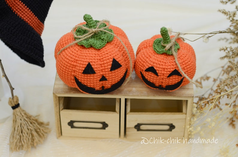 May include: Two crocheted orange pumpkins with black eyes and mouths, sitting on a wooden shelf with a label that says "Dchik-chik handmade".