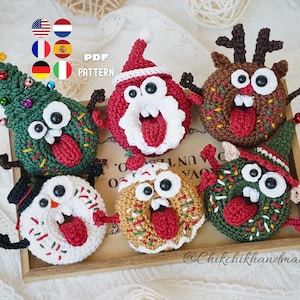 May include: Six crocheted Christmas-themed donut ornaments with googly eyes and protruding tongues. The set includes a tree, Santa, reindeer, snowman, gingerbread, and elf design. The image features the text PDF PATTERN and @Chikchikhandmade.
