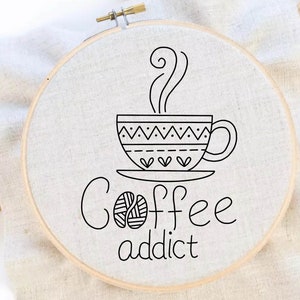 May include: Embroidered hoop art with a black and white illustration of a coffee cup with steam rising from it. The text "Coffee addict" is written below the cup.