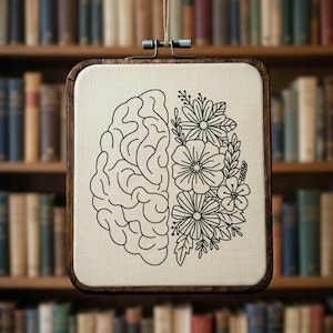 May include: A square, wooden embroidery hoop with a canvas insert. The design is split in half, with a brain outline on the left and floral elements on the right. The artwork is in black and white, and the background is a blurred bookshelf.