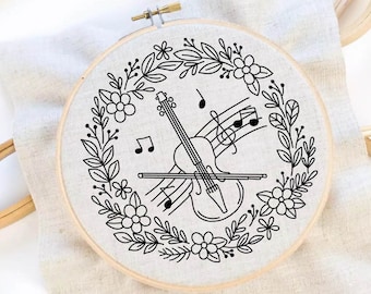Könnte beinhalten: Ein schwarzer und weißer Stickrahmen mit einem floralen Kranzdesign, der eine Geige und Noten umgibt.