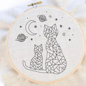 May include: Embroidered hoop art featuring two geometric cats with a crescent moon and stars in the background.