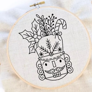 Könnte beinhalten: Schwarz-weiß-Zeichnung eines Nussknackers mit einem Zuckerrohr und Stechpalme auf seinem Hut. Der Nussknacker trägt einen Hut mit einem Stern und einer Schneeflocke. Der Nussknacker hat einen Schnurrbart und einen Bart.