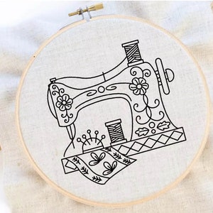 Può includere: Un telaio da ricamo con un disegno a tratto nero di una macchina da cucire vintage. Il disegno include dettagli floreali, rocchetti di filo e un cuscinetto per spilli. Il tessuto è beige chiaro e il telaio è in legno.
