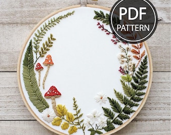 May include: An embroidered hoop art piece featuring a woodland theme. The design includes red-capped mushrooms, green ferns, and various flowers and leaves. The text "PDF PATTERN" is displayed on the upper right. The embroidery is set in a wooden hoop.