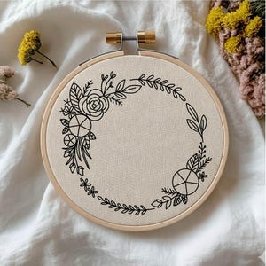 Könnte beinhalten: Ein Stickrahmen mit beigefarbenem Stoff, verziert mit einem schwarzen Blumendesign. Das Design umfasst eine Rose, Blätter und geometrische Formen. Der Holzrahmen hat eine Messingschraube zur Einstellung.