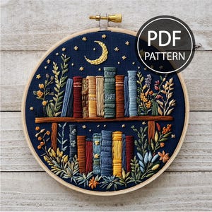 Puede incluir: Arte de bordado en aro que presenta una estantería con libros, una luna creciente y estrellas sobre un fondo azul oscuro. La estantería está rodeada de bordado floral verde y azul.
