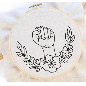 May include: Black and white embroidery hoop with a design of a raised fist with flowers and leaves around it.