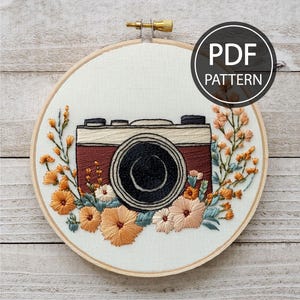 May include: Embroidered hoop art featuring a vintage camera with a brown and white design surrounded by orange, yellow, and blue flowers.