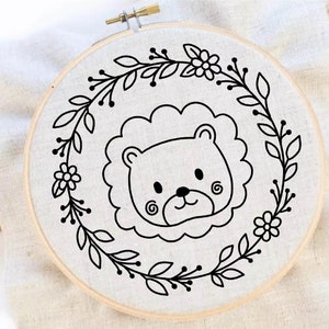 May include: A black and white embroidery hoop with a cute lion face design surrounded by a floral wreath.