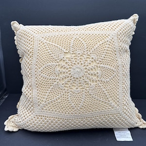 Pode incluir: Almofada quadrada de crochê creme com um design circular central e bordas onduladas. A almofada apresenta um padrão detalhado de trabalho aberto, mostrando o artesanato do item feito à mão. A almofada tem aproximadamente 40 cm quadrados.