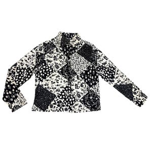 Può includere: Una camicia a maniche lunghe con un design patchwork. La camicia presenta una varietà di motivi floreali in bianco e nero, disposti in un motivo geometrico. La camicia ha un'abbottonatura frontale e un colletto.