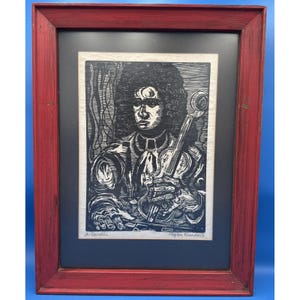 May include: A framed black and white woodcut print depicting a person with long curly hair holding a violin. The artwork is titled A. Corelli and signed by the artist, Bytom Randall. The print is set within a distressed red wooden frame.