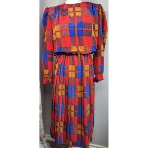 May include: A vintage midi dress with a striking checkerboard design in red, blue, and gold. The dress has long sleeves, a gathered waist, and a pleated skirt. The fabric is lightweight.